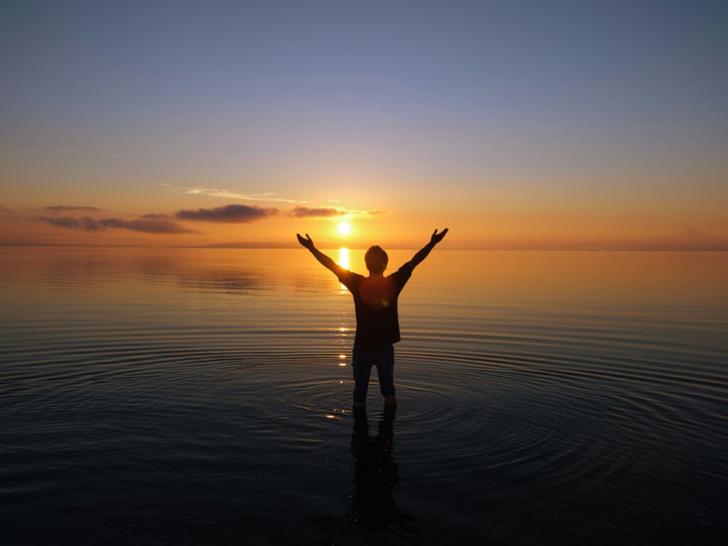 nonprofit brand refresh. 
photo of a person standing water with arms raised, watching the sunrise.